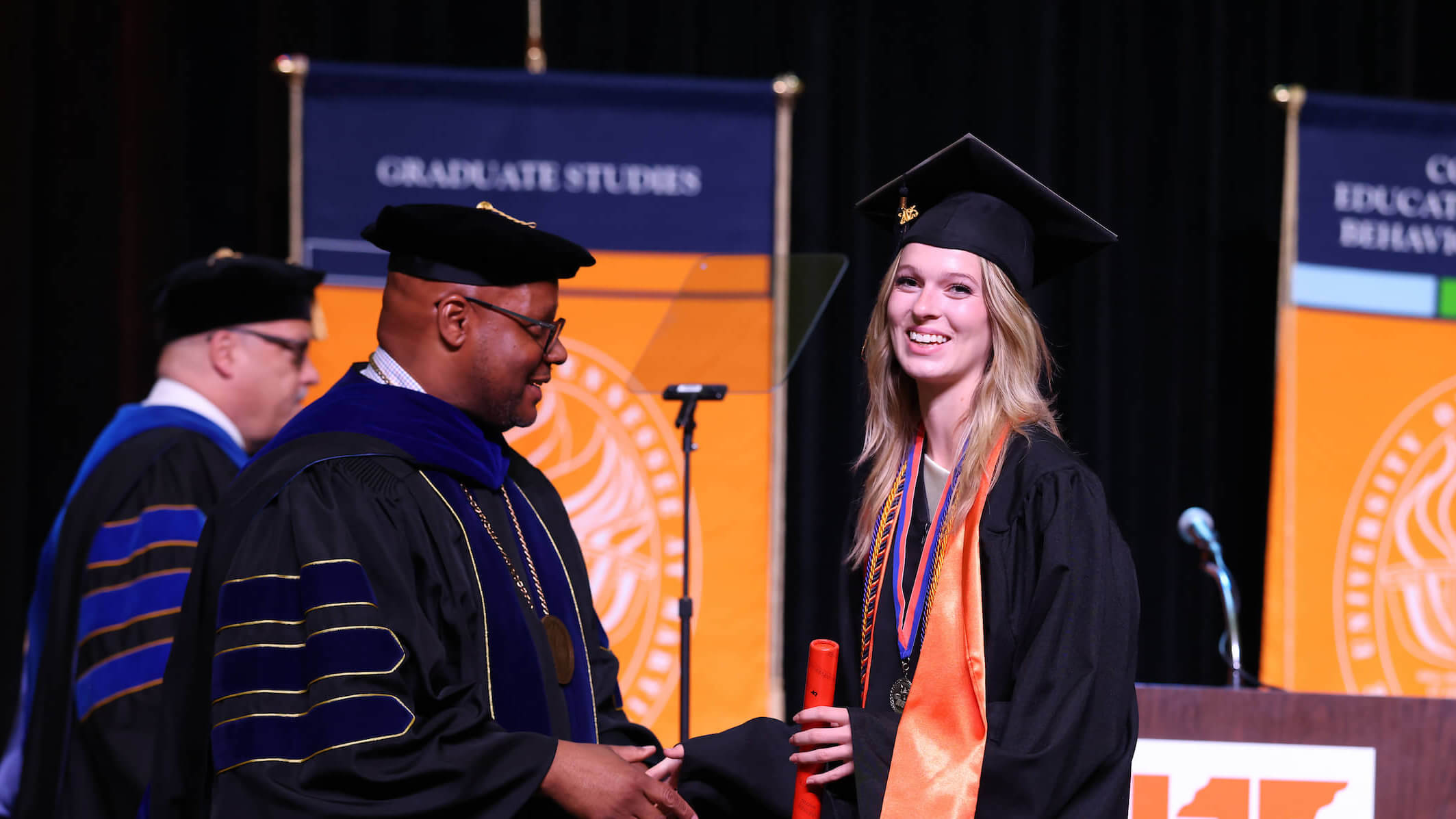 Graduate receives diploma, shaking hands with university official on stage during UT Martin commencement ceremony.