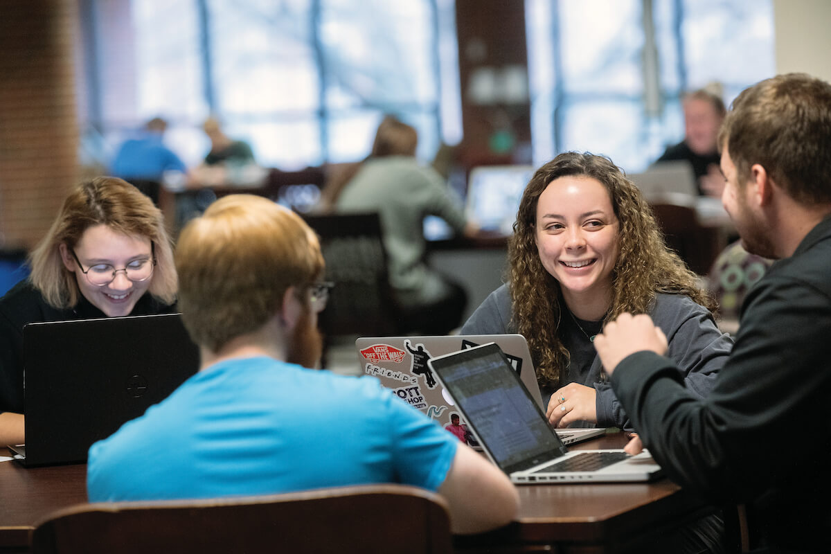 Students talking and studying in the library with laptops and textbooks.