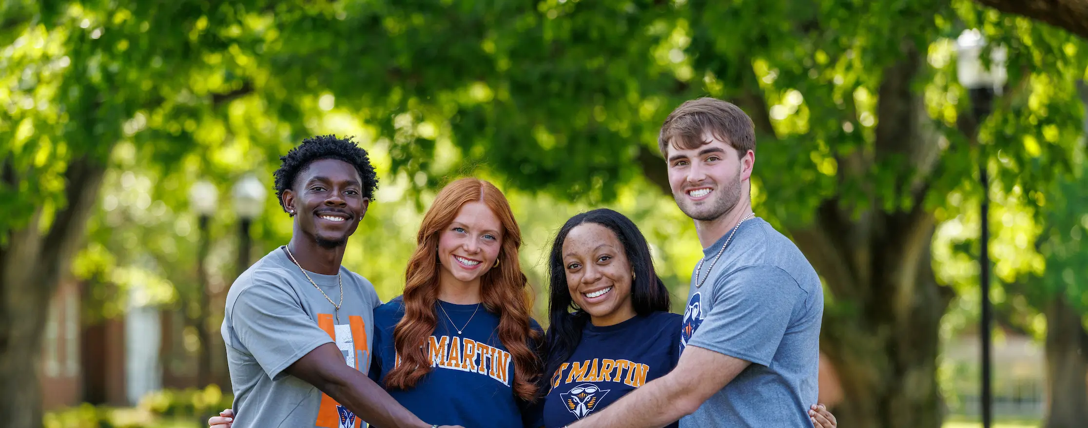 Four smiling students with their arms over each other shoulders.