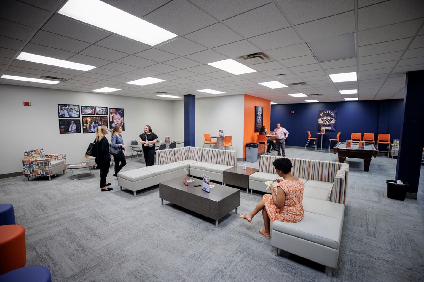 Students and staff talking inside a large navy blue and orange room.