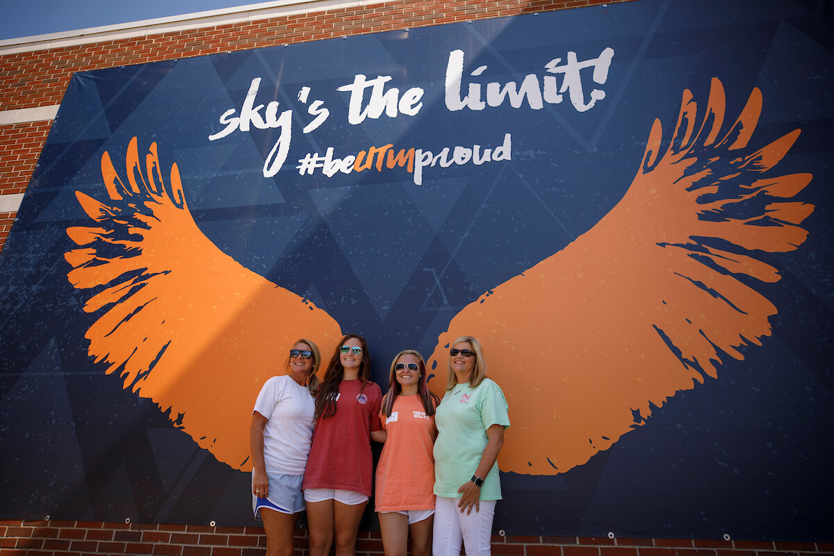Four students stand in front of the raised wings of the Sky's the Limit mural.