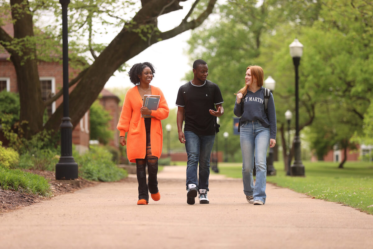 Three students talk as they walk across the quad